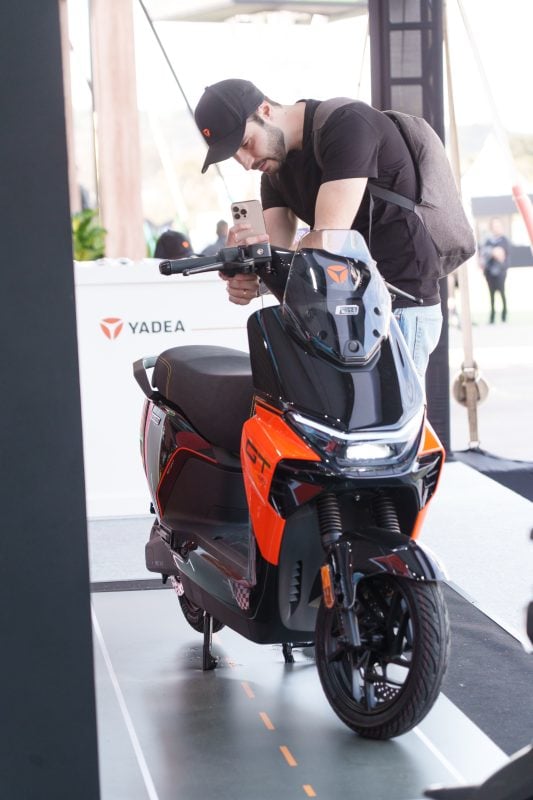 Attendee photographing an orange and black YADEA GS70 PRO at the YADEA exhibition booth