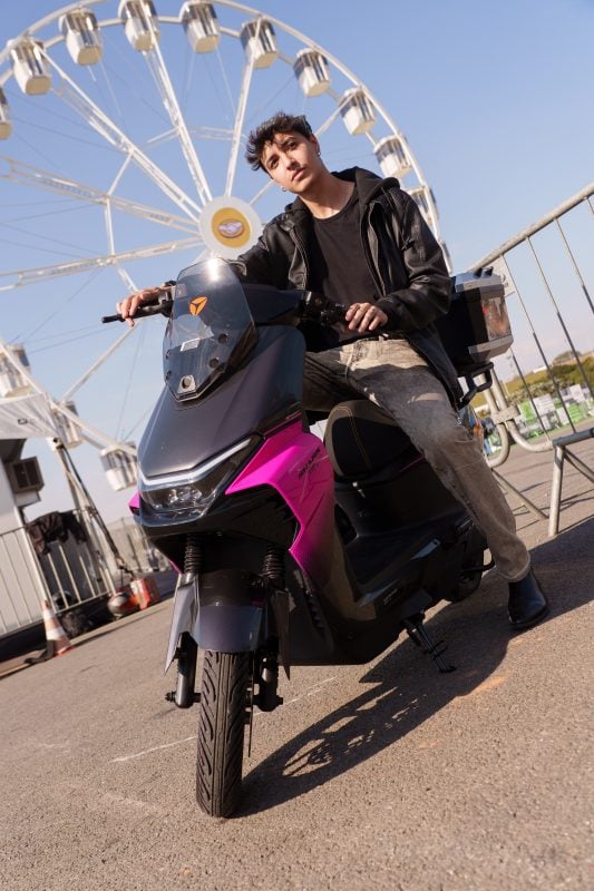 Visitor seated on a pink and black YADEA GS70 PRO near the Festival Interlagos Ferris wheel